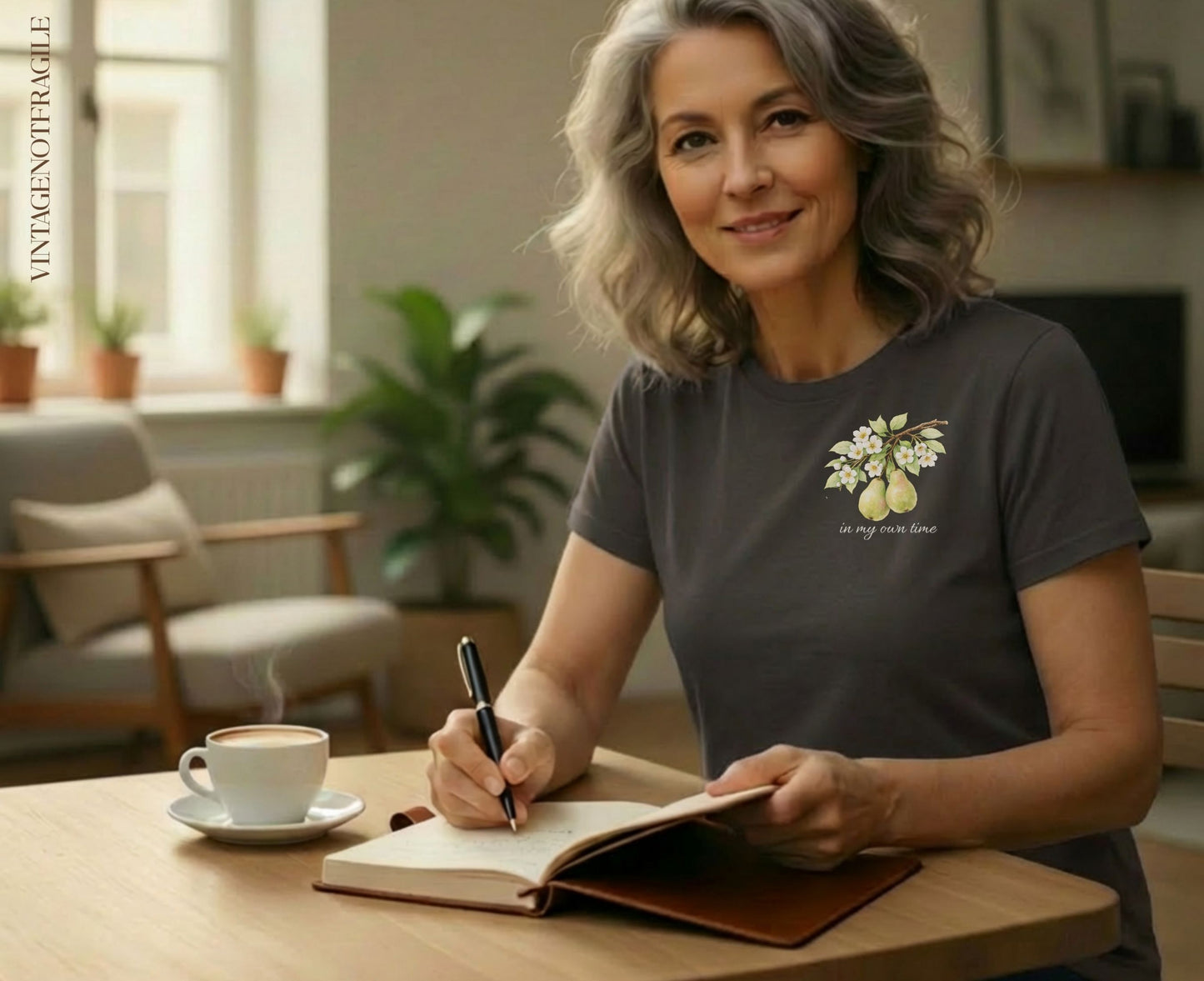 Woman in dark t-shirt with pear branch design writing at a desk.