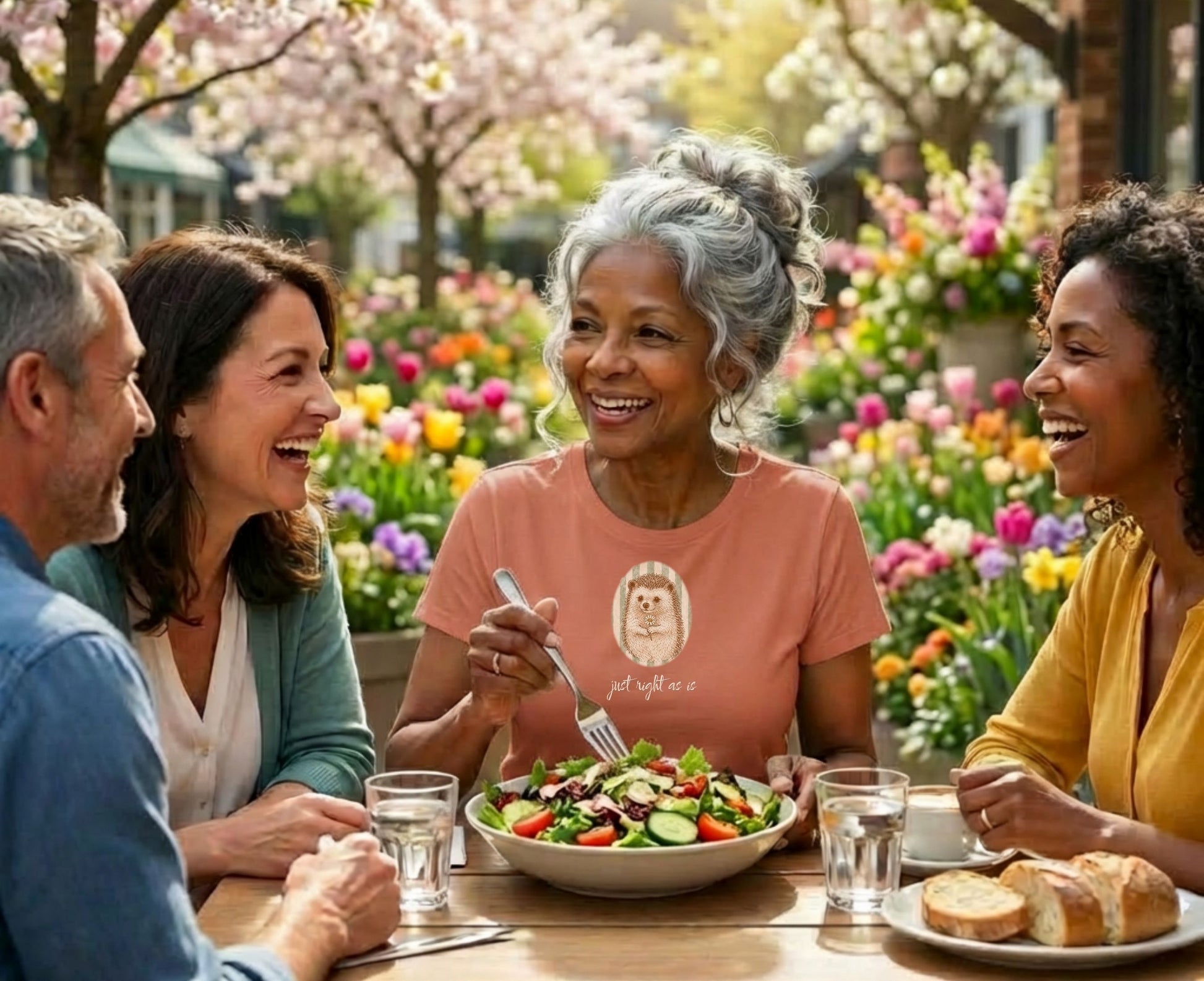 Woman in orange t-shirt with hedgehog graphic smiles while eating salad outdoors.