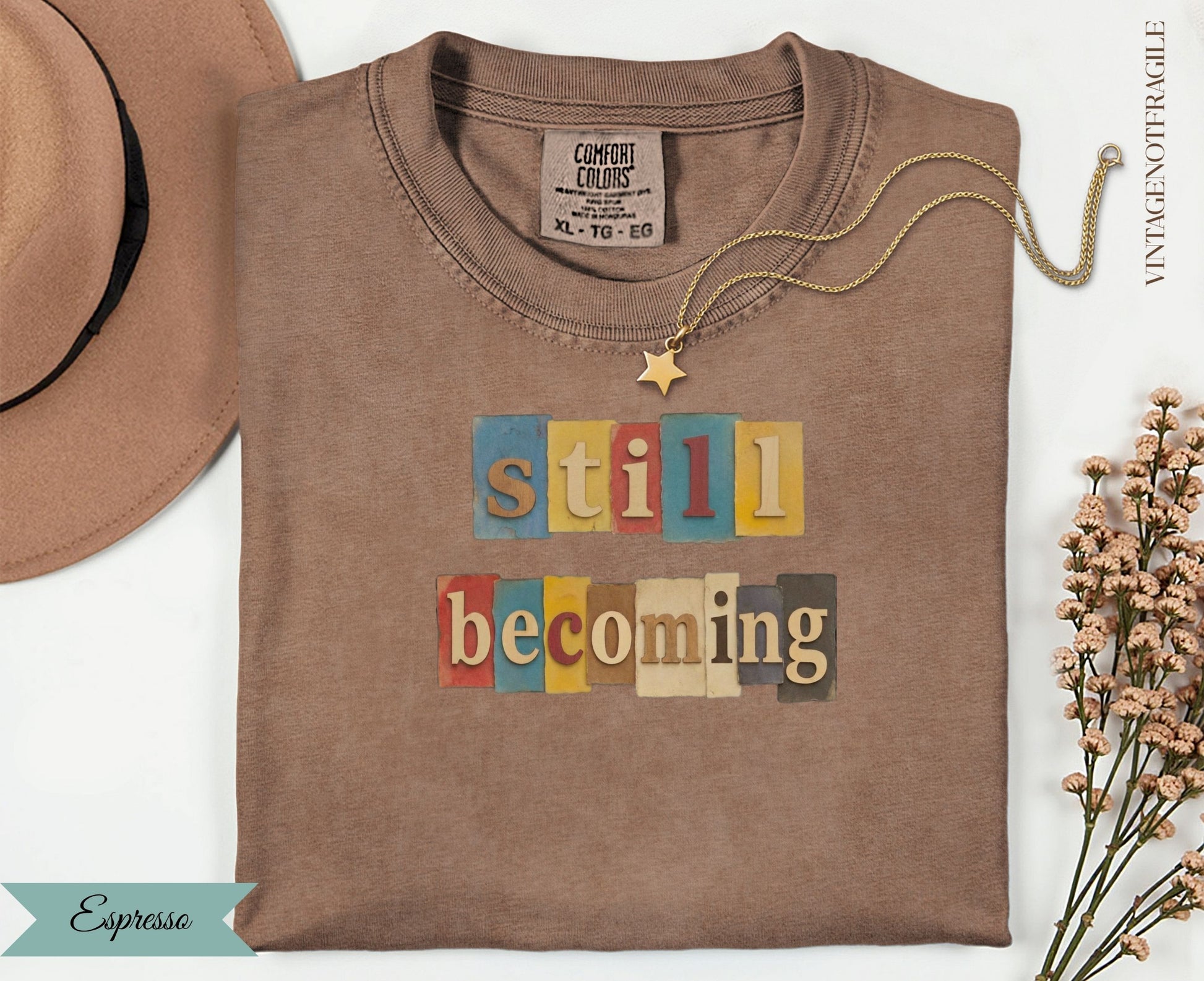 Espresso t-shirt with colorful "still becoming" text graphic.
