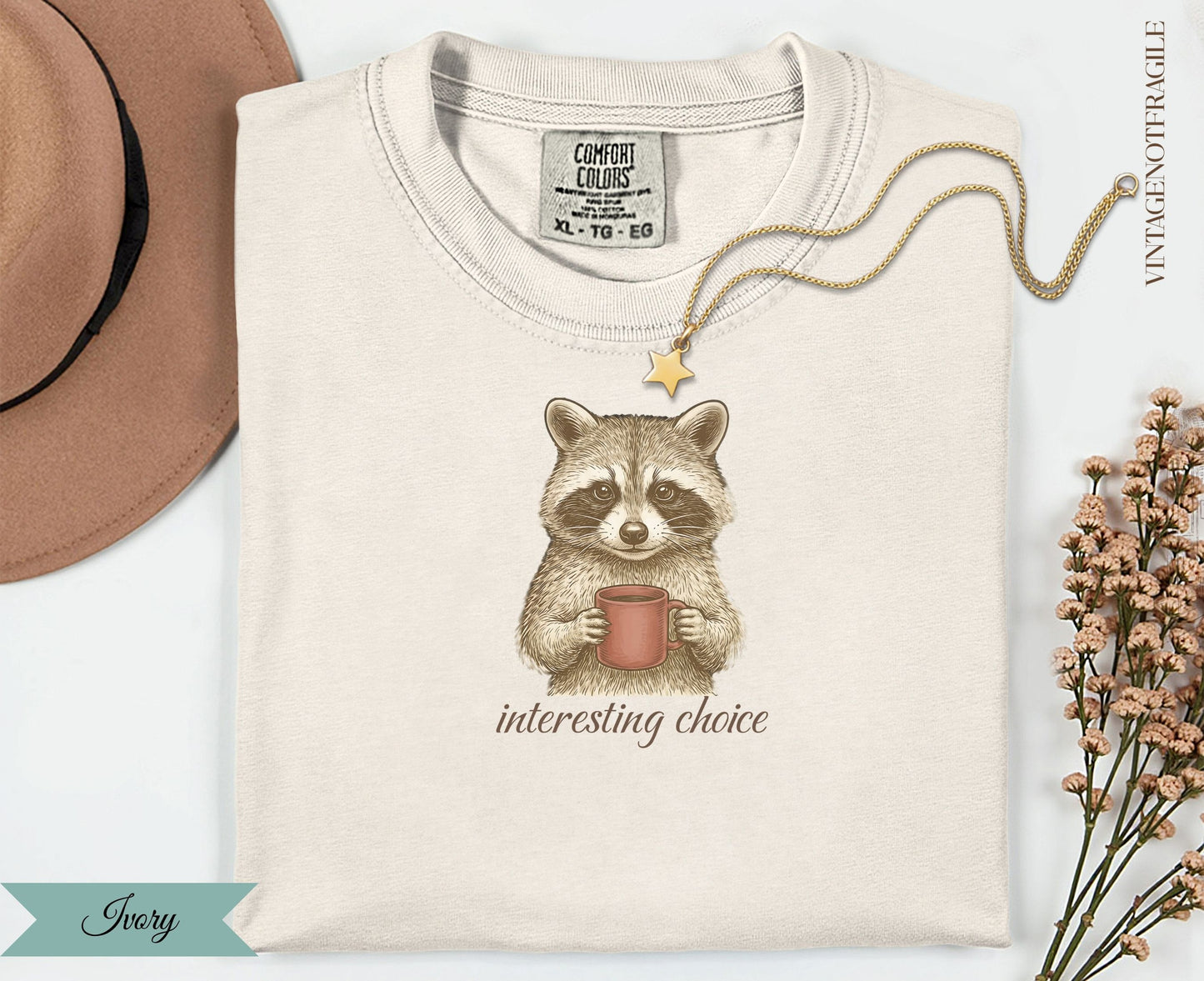 Ivory t-shirt with raccoon holding coffee cup, "interesting choice" text.