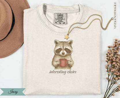 Ivory t-shirt with raccoon holding coffee cup, "interesting choice" text.