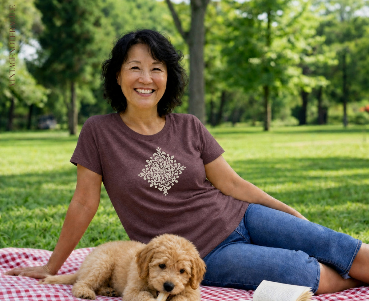 Woman and puppy on picnic blanket in park, woman wears brown shirt with design.