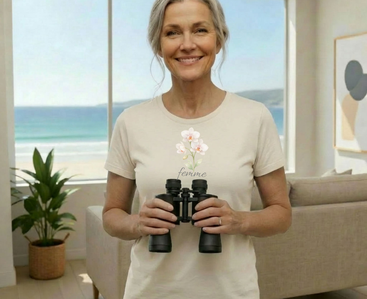 Woman wearing a cream t-shirt with "femme" and orchids, holding binoculars.
