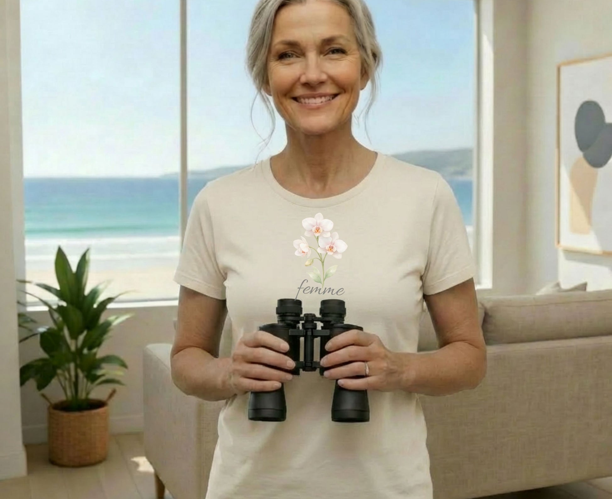 Woman wearing a cream t-shirt with "femme" and orchids, holding binoculars.