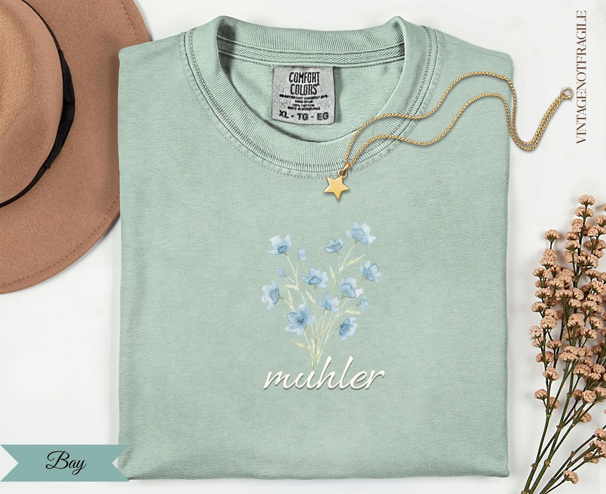 Pale green t-shirt with blue flowers and "muhler" text, with gold necklace.