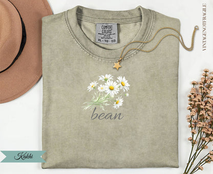 Khaki t-shirt with a bouquet of white daisies and "bean" text.