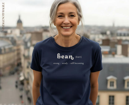 Woman wearing a navy t-shirt with "bean (ban), strong, steady, still becoming" text.