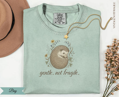 Sage green t-shirt with hedgehog graphic and "gentle. not fragile." text.