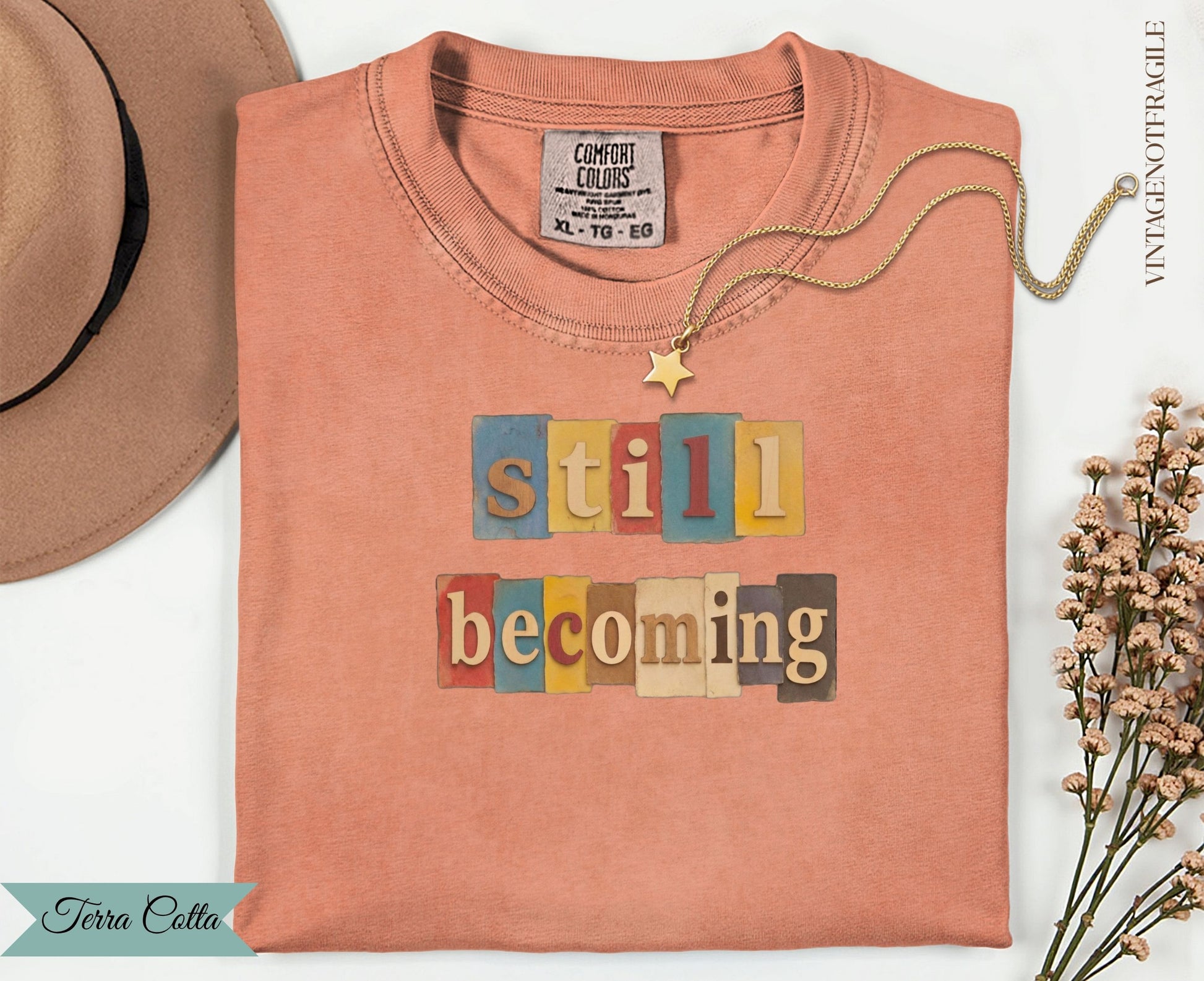Still Becoming graphic tee with colorful block letters on a peach t-shirt.