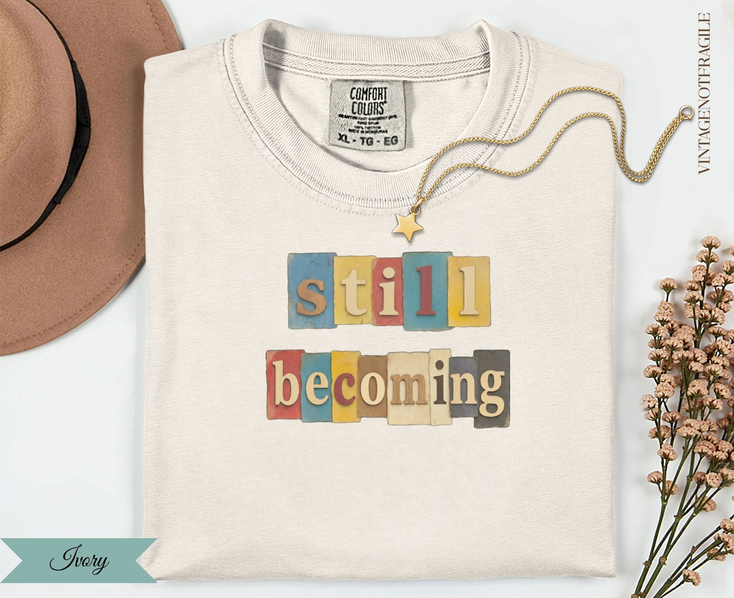 Cream t-shirt with "still becoming" text in colorful block letters.
