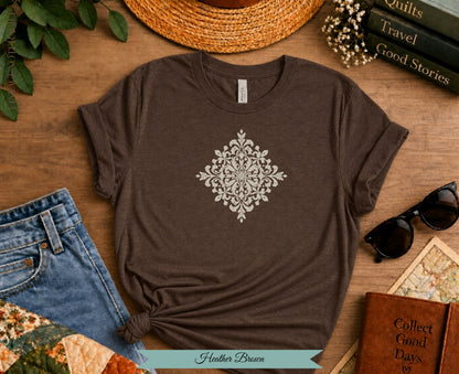 Heather Brown t-shirt with ornate white medallion graphic on wooden background.