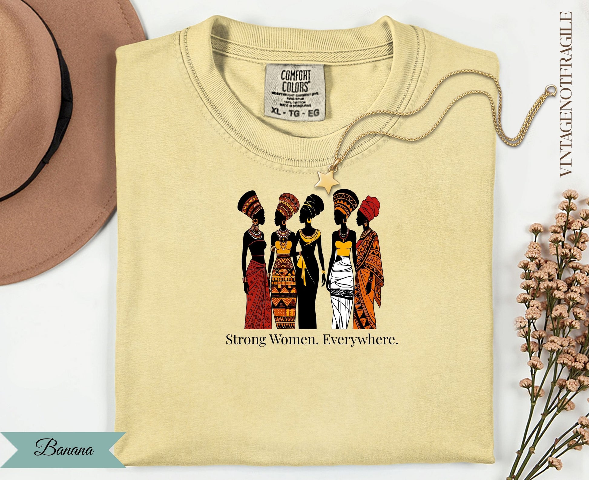 Cream t-shirt with graphic of five women in traditional African attire, text "Strong Women. Everywhere."