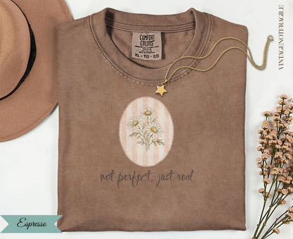 Espresso colored t-shirt with daisy graphic and "not perfect, just real" text.