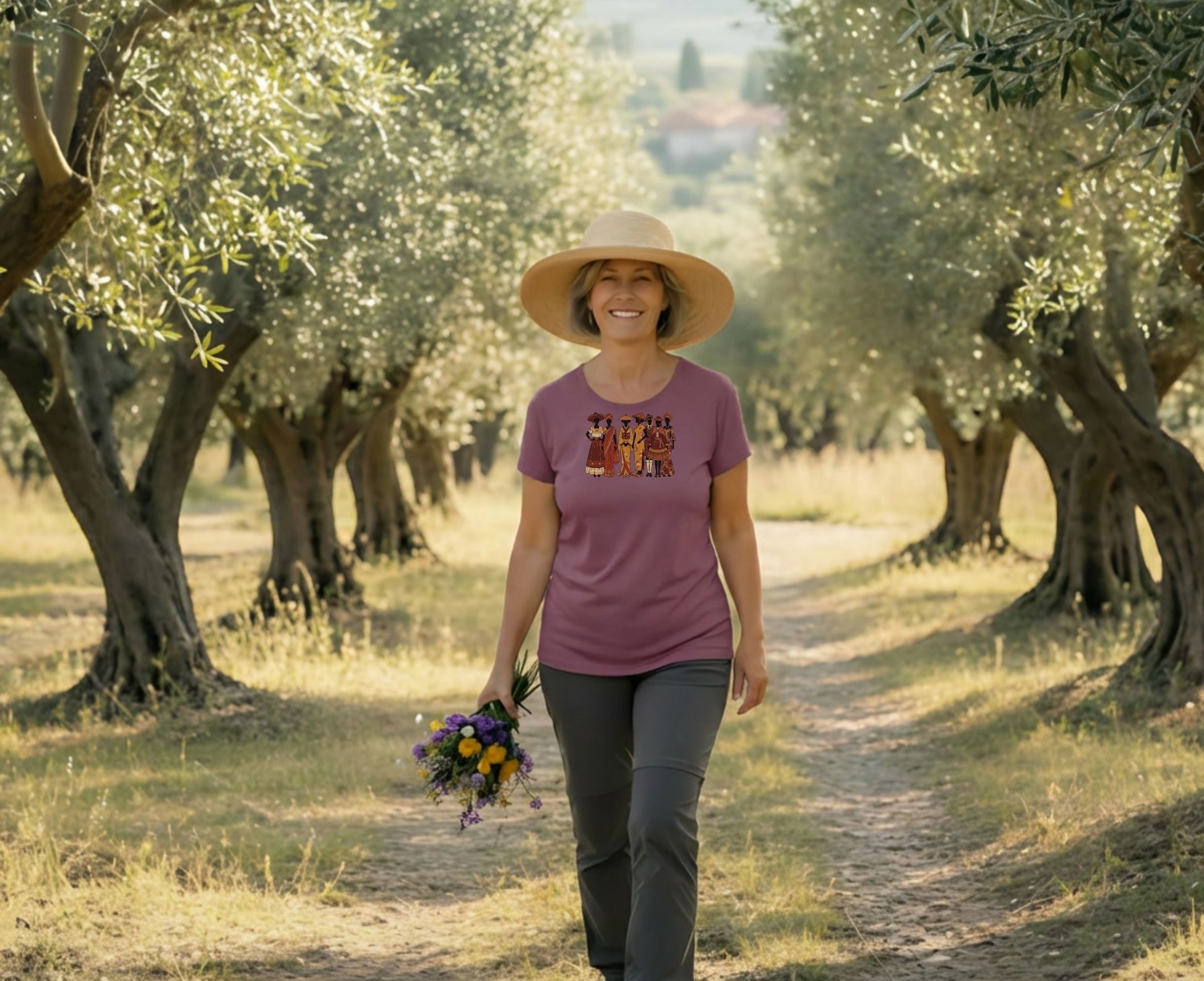 Woman in olive grove wearing t-shirt with group of people, holding flowers.