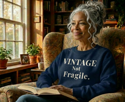 Elderly woman in armchair wearing "Vintage Not Fragile" sweatshirt, reading a book.