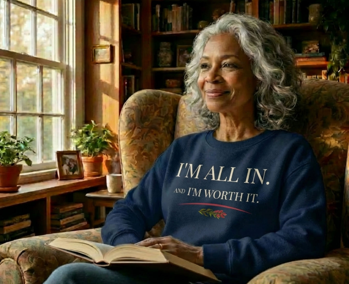 Elderly woman in armchair wearing navy sweatshirt with "I'M ALL IN. AND I'M WORTH IT."