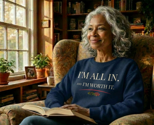 Elderly woman in armchair wearing navy sweatshirt with "I'M ALL IN. AND I'M WORTH IT."