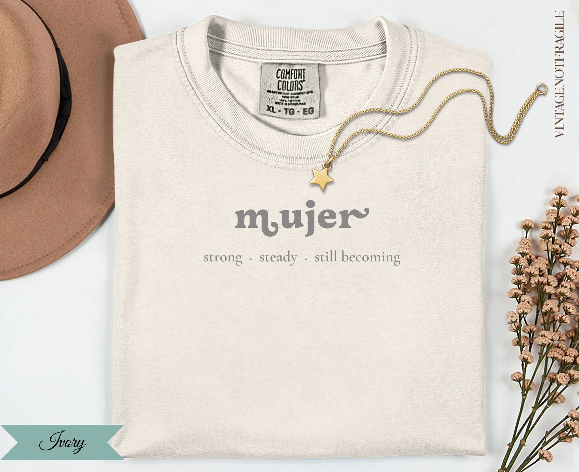 Ivory t-shirt with "mujer strong steady still becoming" text and gold necklace.