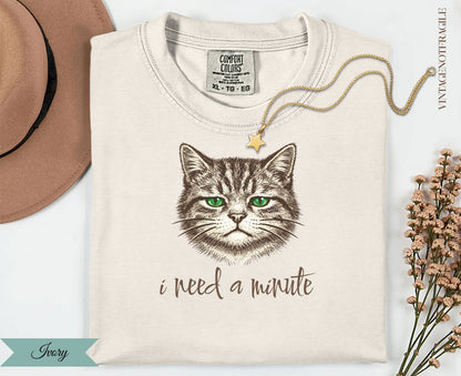 Cream t-shirt with a drawing of a grumpy cat and the text "i need a minute".