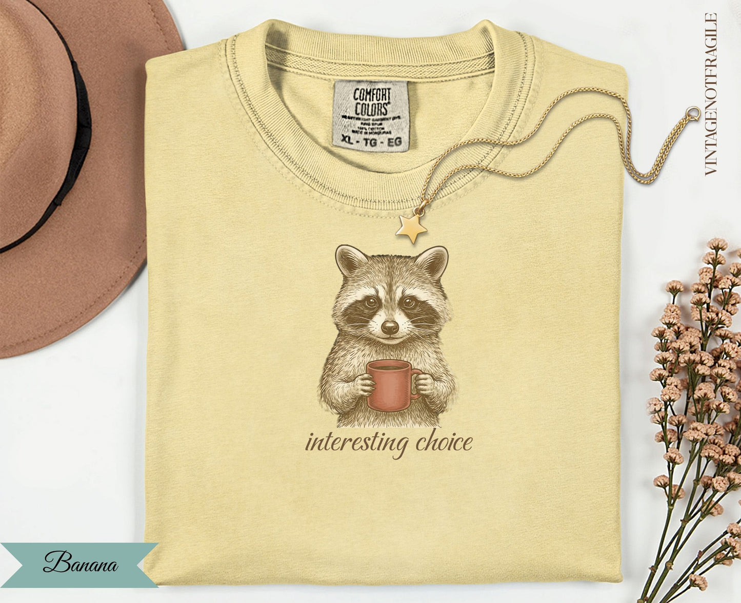 Cream t-shirt with a raccoon holding a coffee mug, "interesting choice" text.