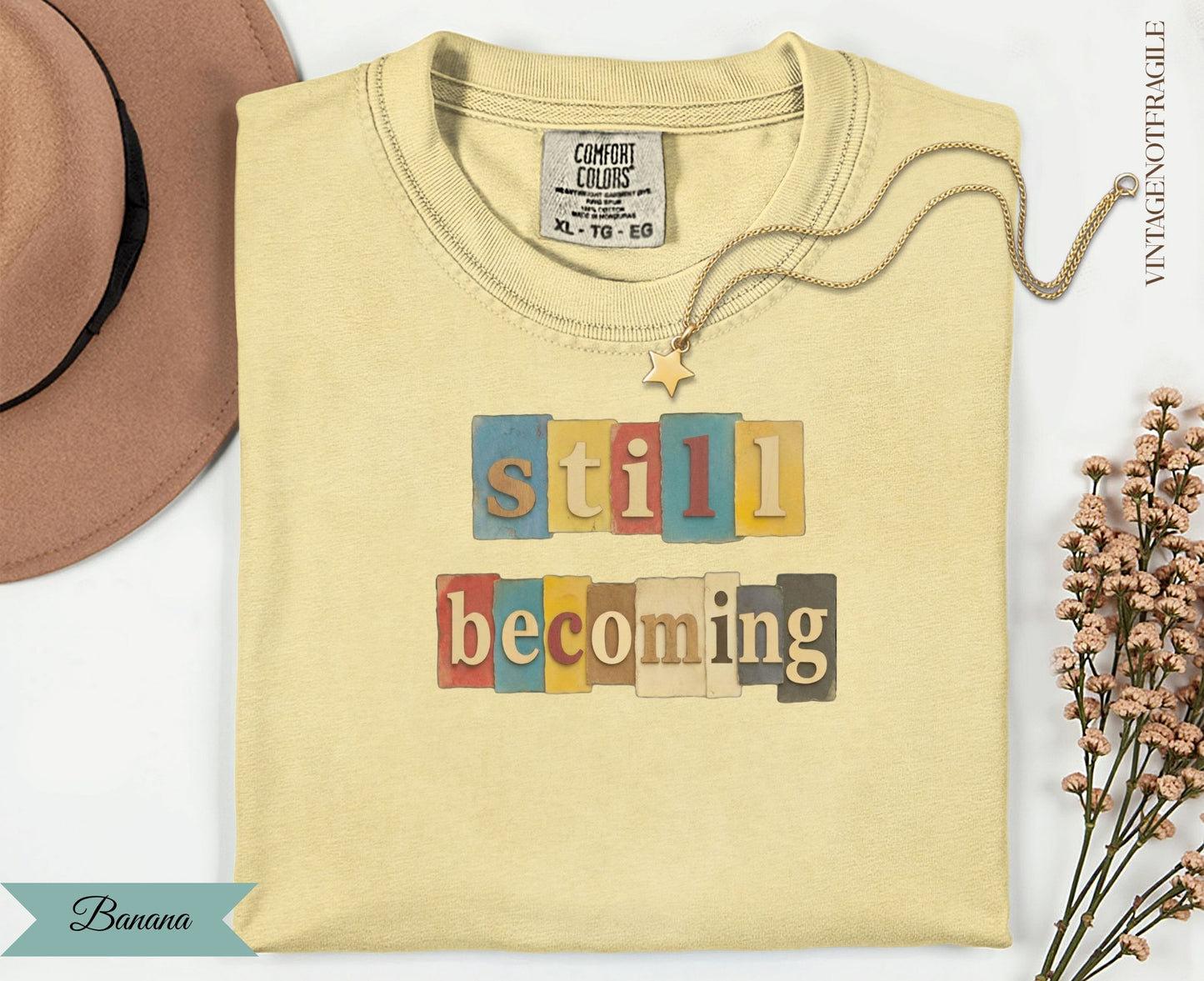 Light yellow t-shirt with "still becoming" text in colorful blocks.