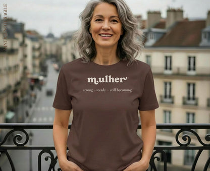 Woman in brown t-shirt with "mulher strong steady still becoming" text.