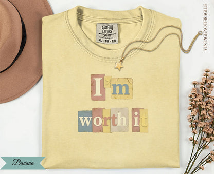 Light yellow t-shirt with "I'm worth it" in pastel blocks and a gold necklace.