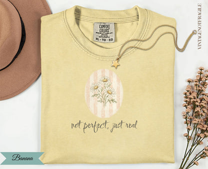 Yellow t-shirt with "not perfect, just real" text and floral graphic.
