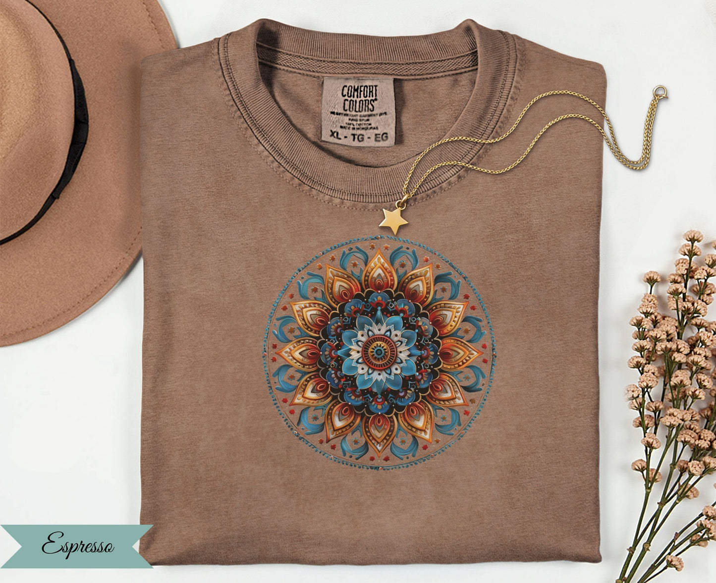 Brown t-shirt with colorful mandala design, gold necklace, and tan hat.
