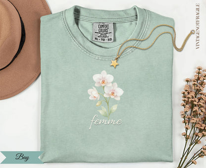Light mint t-shirt with "femme" and orchid graphic, gold necklace.