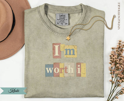T-shirt with "I'm worth it" text in pastel blocks, gold necklace, and dried flowers.