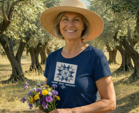 Woman in straw hat wearing blue t-shirt with quilt square, holding flowers.