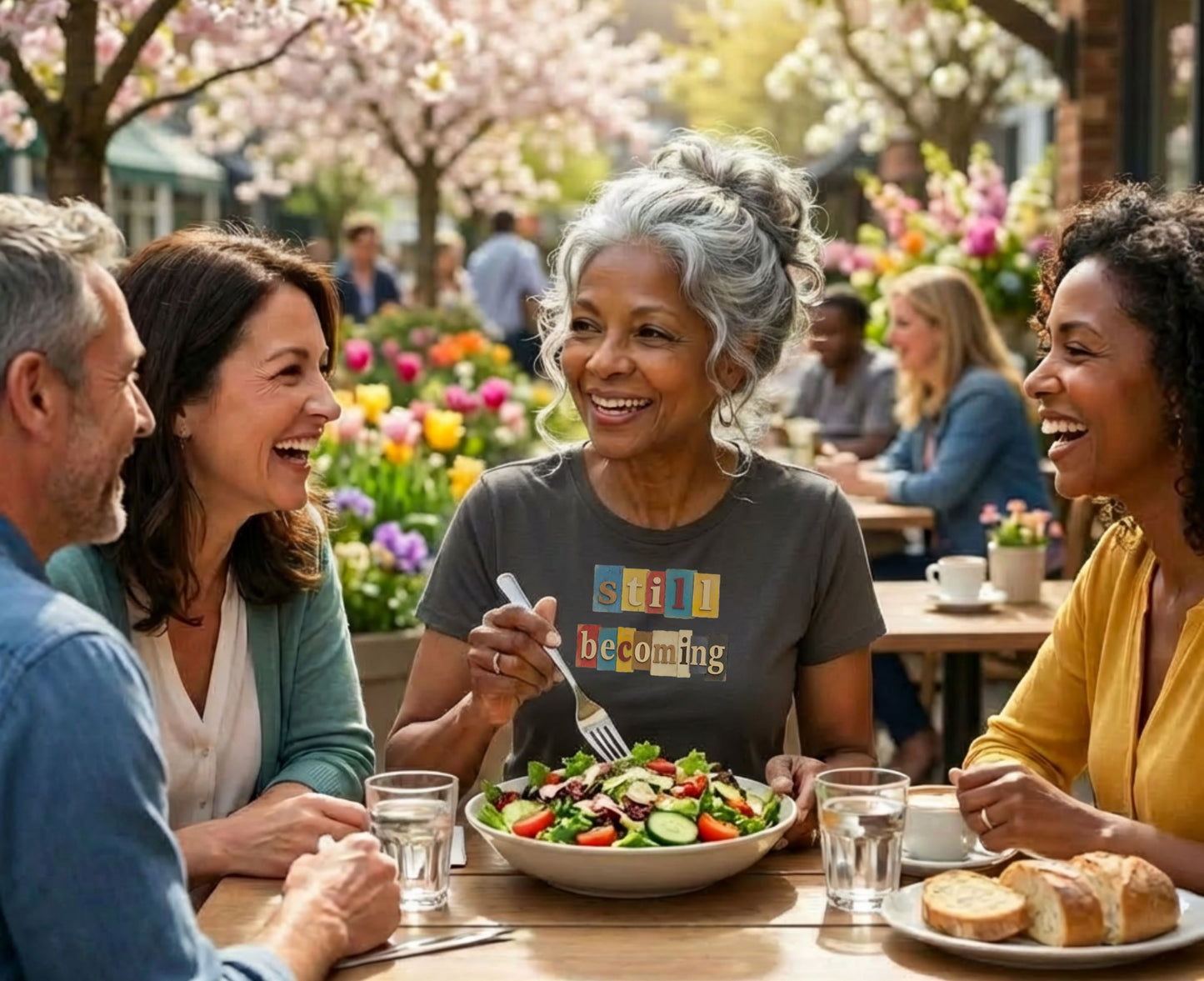 Four people laugh around a table with salad and bread.