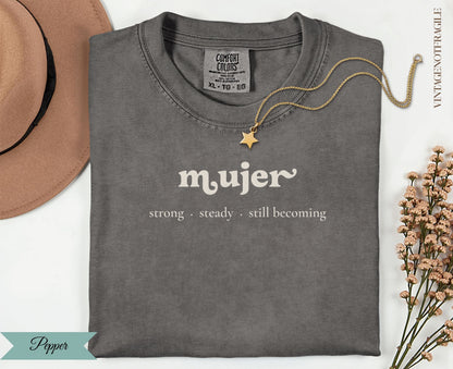 Grey t-shirt with "mujer strong steady still becoming" text and gold necklace.