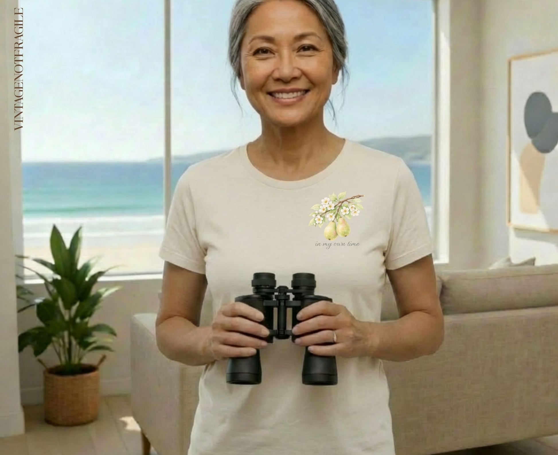 Woman holding binoculars, wearing a t-shirt with pear branch graphic and text "in my own time".