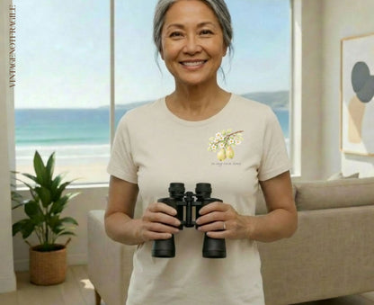 Woman holding binoculars, wearing a t-shirt with pear branch graphic and text "in my own time".