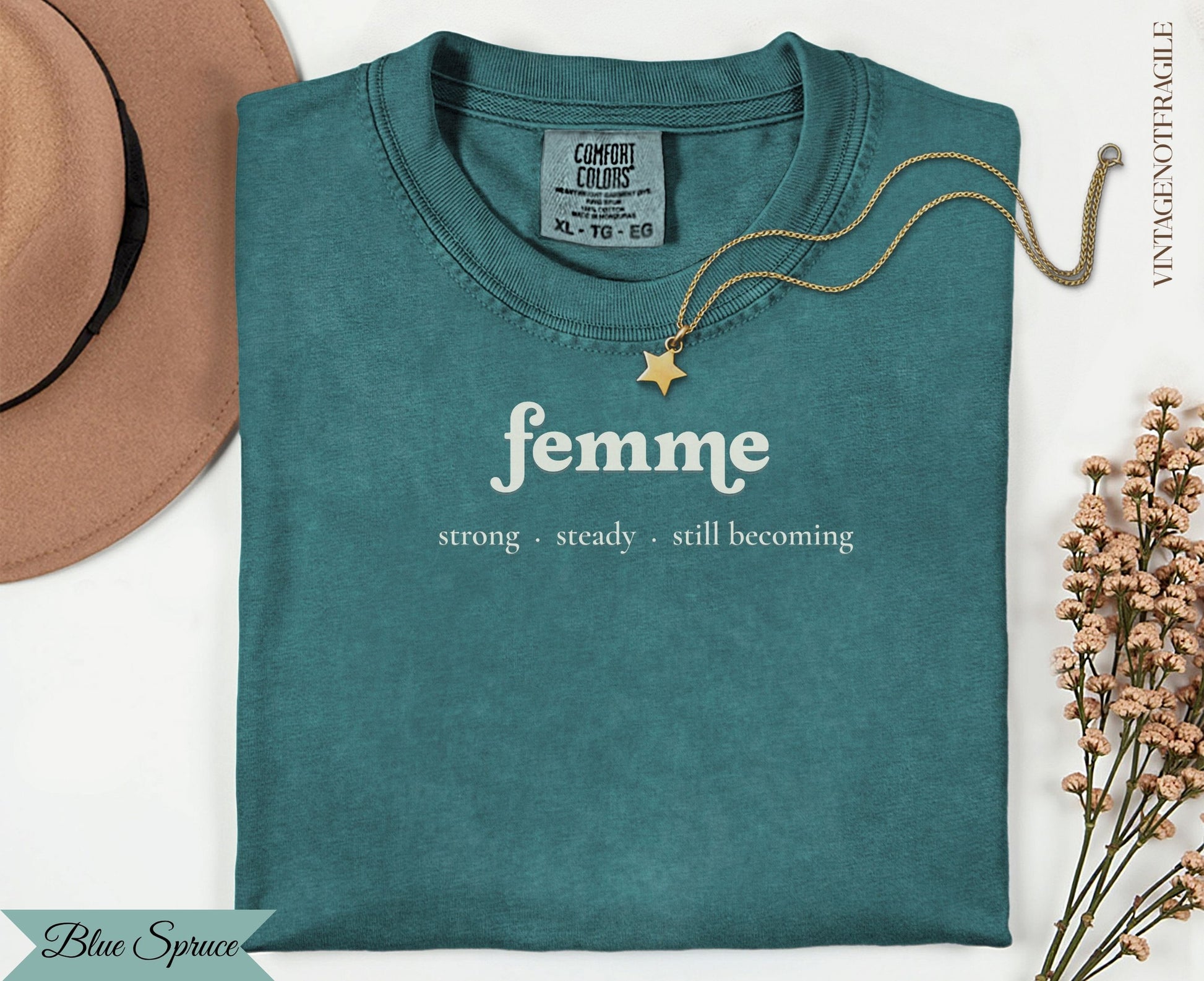 Teal t-shirt with "femme strong steady still becoming" text and gold necklace.