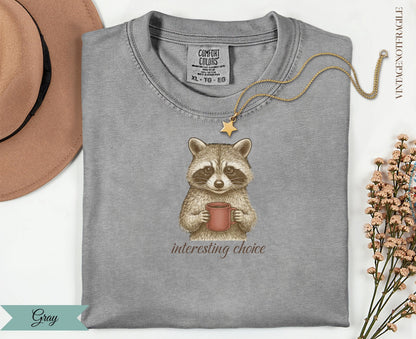 Gray t-shirt with raccoon holding coffee cup, "interesting choice" text.