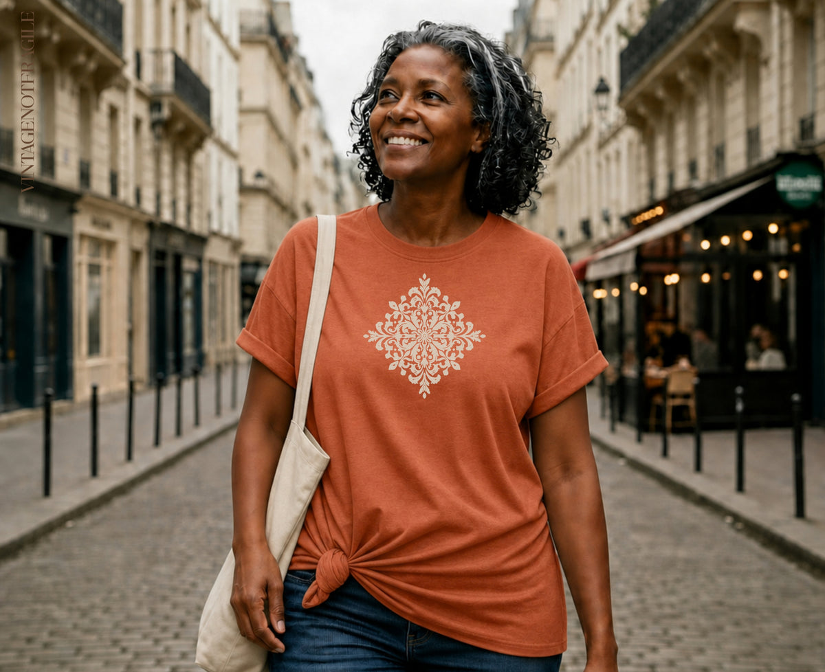 Woman wearing orange t-shirt with white mandala design, carrying tote bag.