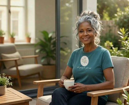 Woman with grey hair sits in chair holding mug, wearing t-shirt with floral graphic.