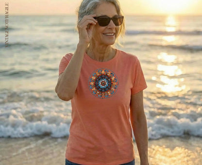 Woman in coral t-shirt with circular mandala design on beach at sunset.