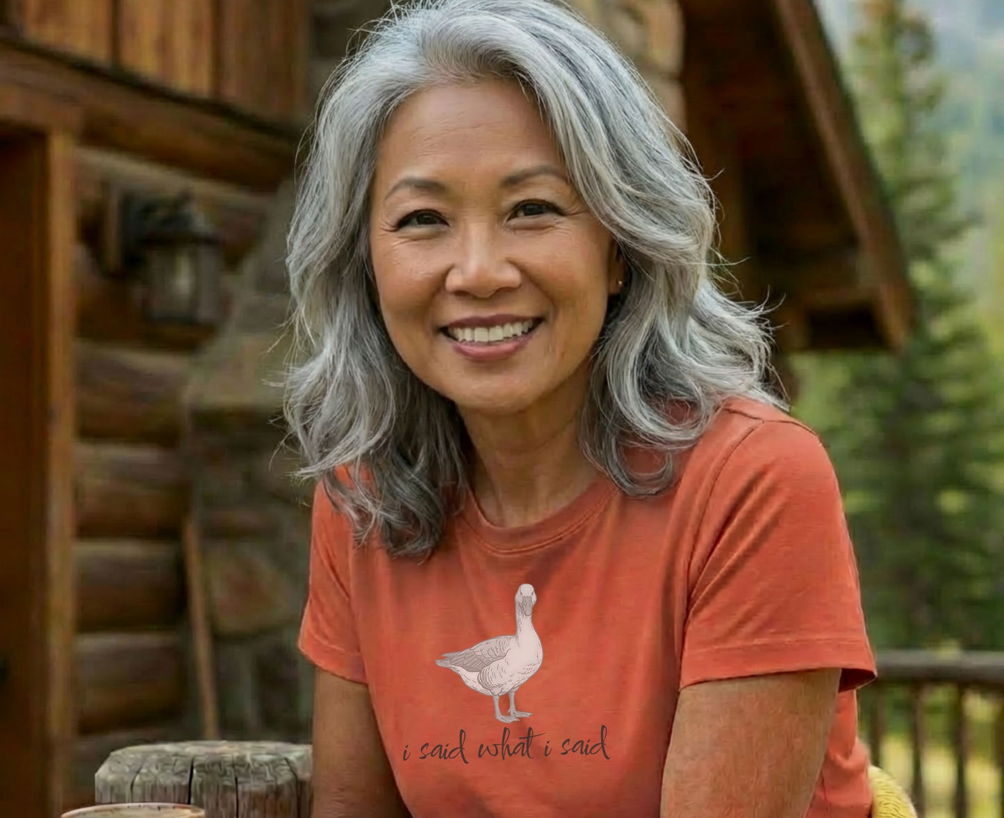 Woman with gray hair smiles wearing an orange t-shirt with a goose and text.