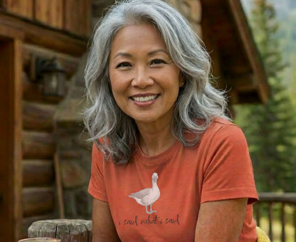 Woman with gray hair smiles wearing an orange t-shirt with a goose and text.