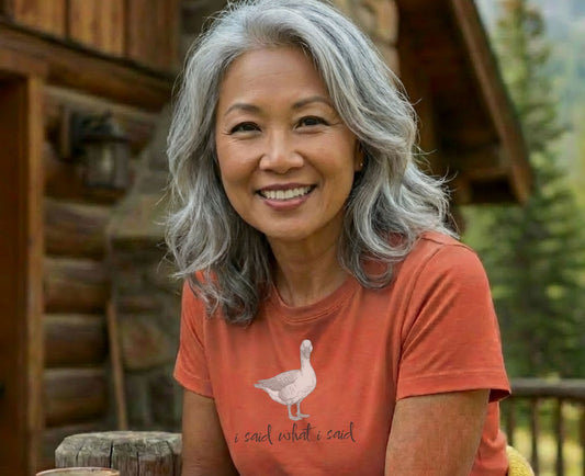 Woman with gray hair smiles wearing an orange t-shirt with a goose and text.