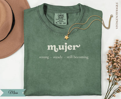 Green t-shirt with "mujer strong steady still becoming" text, gold necklace.