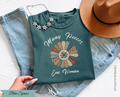 Teal t-shirt with "Many Pieces. One Woman." floral graphic and "Blue Spruce" label.