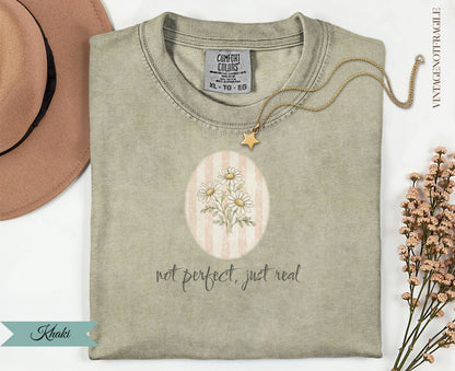 Khaki t-shirt with daisy graphic and "not perfect, just real" text.