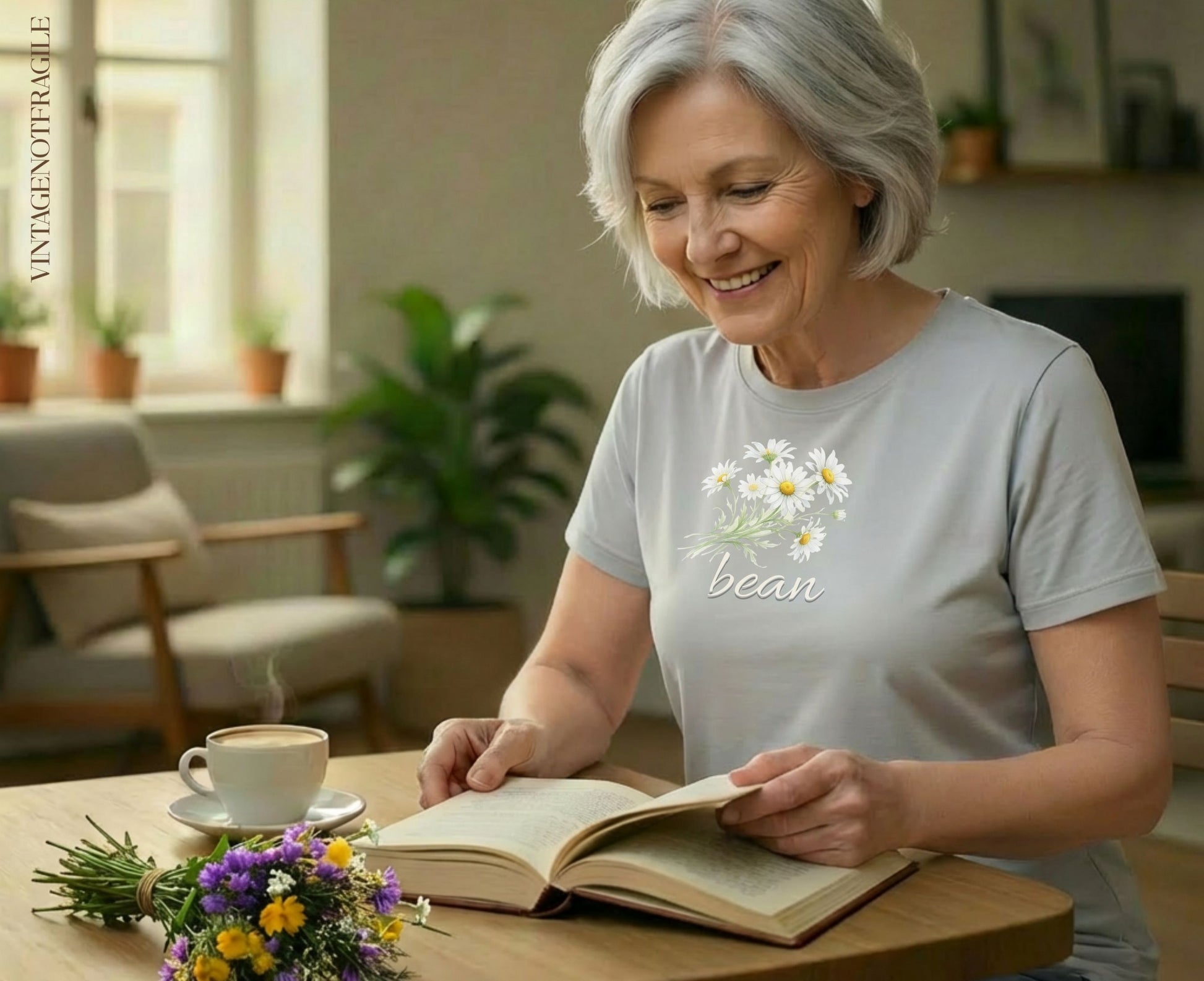 Gray t-shirt with embroidered daisies and "bean" text worn by a woman reading.
